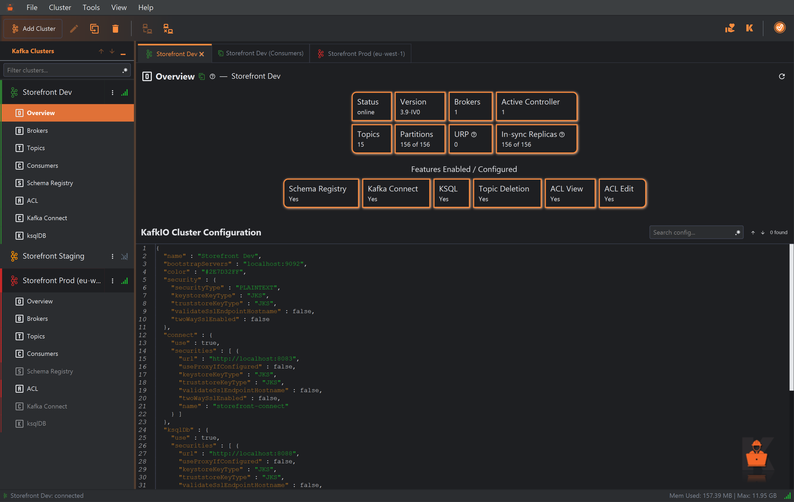 The Overview of the Storefront Dev cluster, in its main tab beside the Storefront Dev (Consumers) and Storefront Prod (eu-west-1) tabs. Cards show Status online, Version 3.9-IV0, Brokers 1, Active Controller 1, Topics 15, Partitions 156 of 156, URP 0 and In-sync Replicas 156 of 156. Under Features Enabled / Configured, Schema Registry, Kafka Connect, KSQL, Topic Deletion, ACL View and ACL Edit all say Yes. Below, KafkIO Cluster Configuration shows the cluster's settings as JSON, with a Search config field at the right.